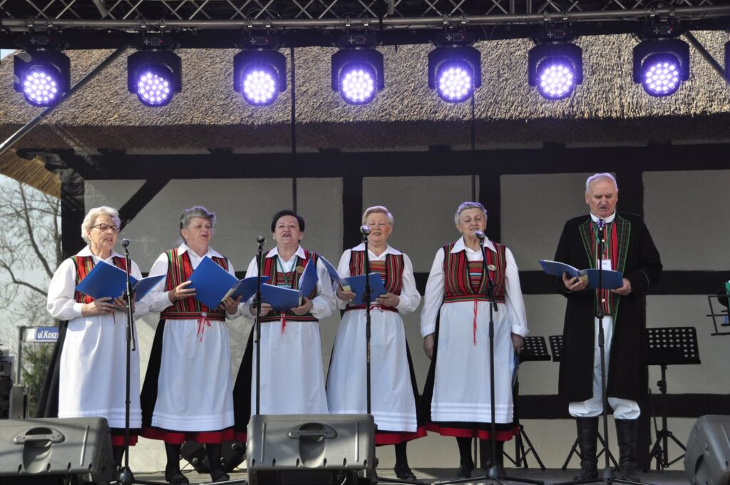 Zespół folklorystyczny – pięć kobiet w tradycyjnych strojach jamneńskich i mężczyzna śpiewają na scenie pod profesjonalnym oświetleniem (kliknięcie powiększy zdjęcie).