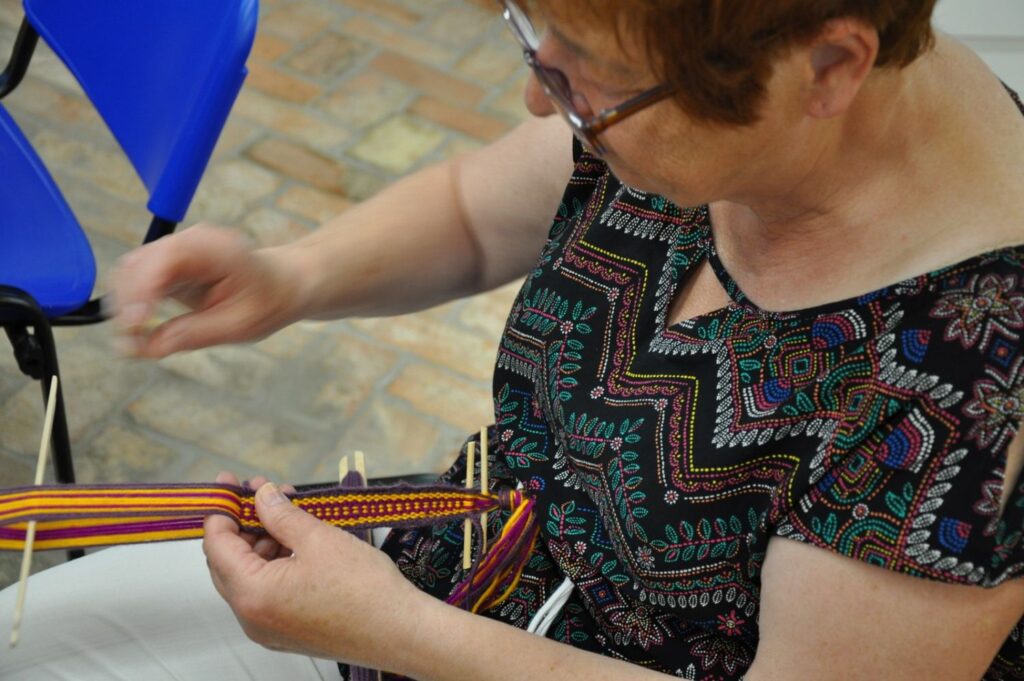 Uczestniczka warsztatów tkania na bardkach przeplata kolorowe nici, tworząc wąski, wzorzysty pas (kliknięcie powiększy zdjęcie).