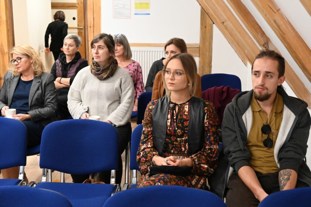 Uczestnicy siedzą w rzędach krzeseł i słuchają wykładu w sali konferencyjnej (kliknięcie powiększy zdjęcie).