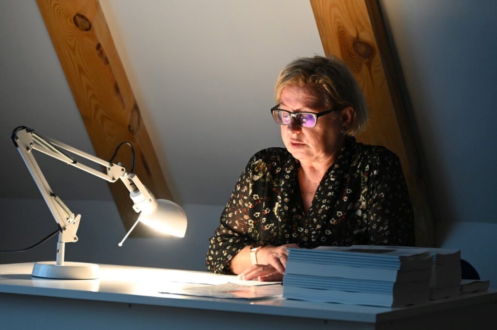 Prelegentka siedzi przy biurku oświetlonym lampką i czyta materiały podczas wykładu (kliknięcie powiększy zdjęcie).