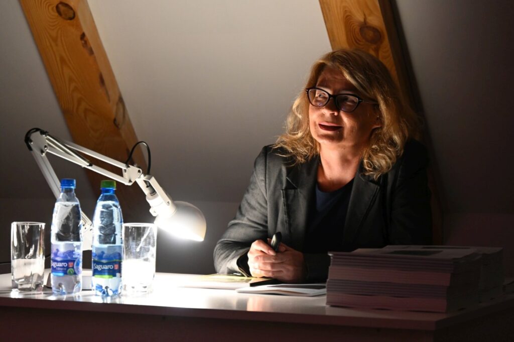 Prelegentka siedzi przy biurku oświetlonym lampką i prowadzi wykład podczas seminarium jamneńskiego (kliknięcie powiększy zdjęcie).