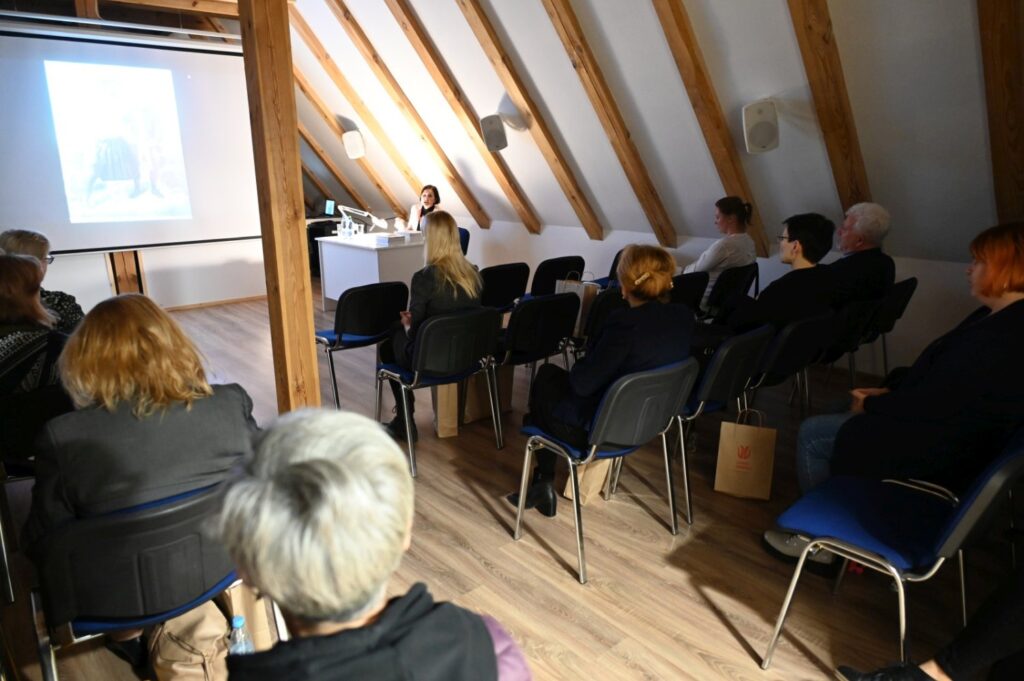 Uczestnicy seminarium siedzą na krzesłach i oglądają prezentację wyświetlaną na ekranie (kliknięcie powiększy zdjęcie).