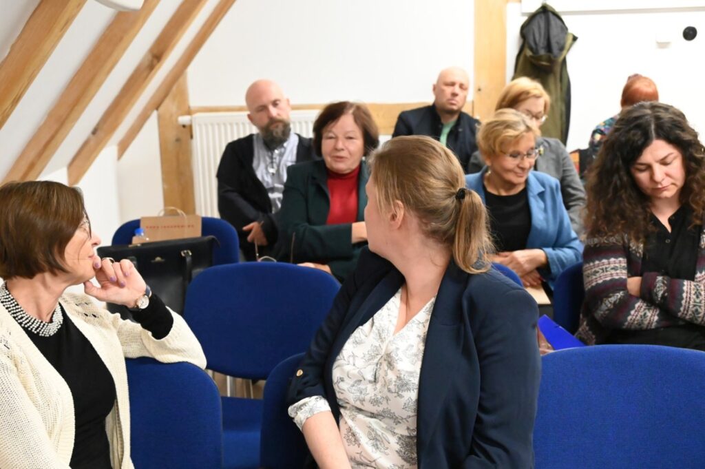 Publiczność siedzi na sali na niebieskich krzesłach, część osób prowadzi dyskusje dotyczące tematyki spotkania (kliknięcie powiększy zdjęcie).