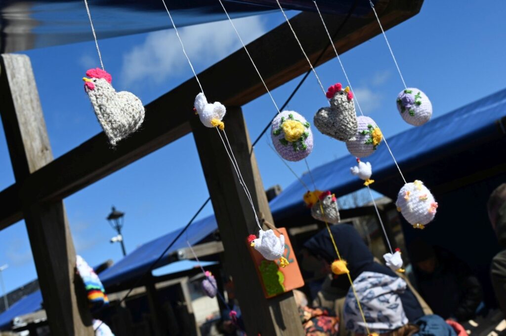 Wiszące wielkanocne ozdoby z wełny i włóczki w kształcie kur i jajek zawieszone na drewnianej konstrukcji (kliknięcie powiększy zdjęcie).