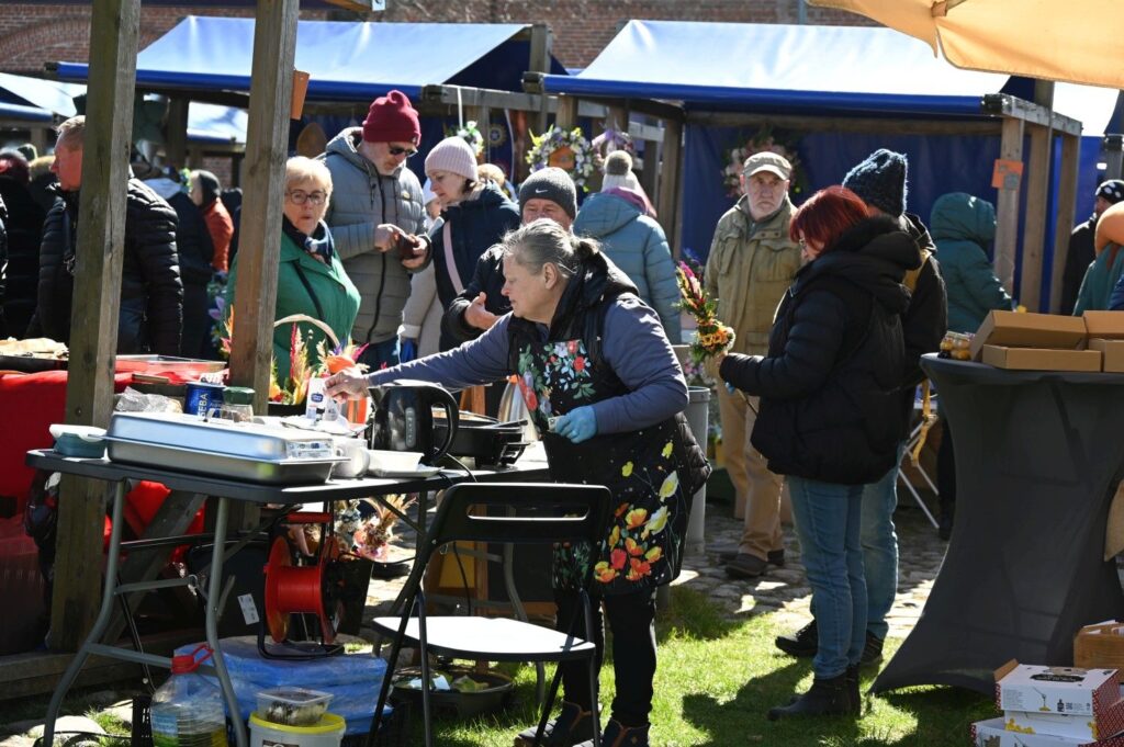 Stoisko z rękodziełem, przy którym sprzedawczyni obsługuje odwiedzających oglądających wyroby podczas jarmarku (kliknięcie powiększy zdjęcie).
