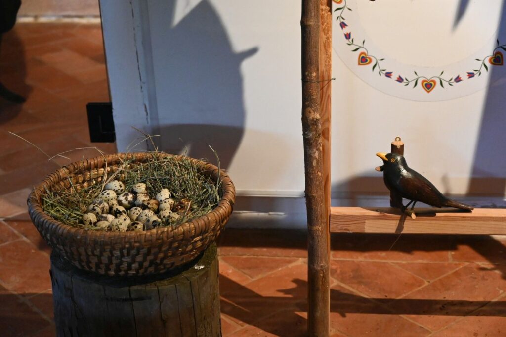 Kosz z przepiórczymi jajkami ustawiony we wnętrzu skansenu obok drewnianych dekoracji z ptakami (kliknięcie powiększy zdjęcie).