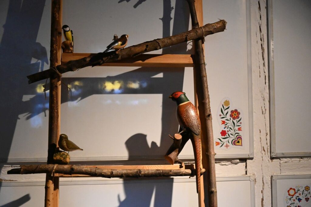 Drewniana półka z ręcznie wykonanymi figurkami ptaków ustawiona we wnętrzu tradycyjnej chaty (kliknięcie powiększy zdjęcie).