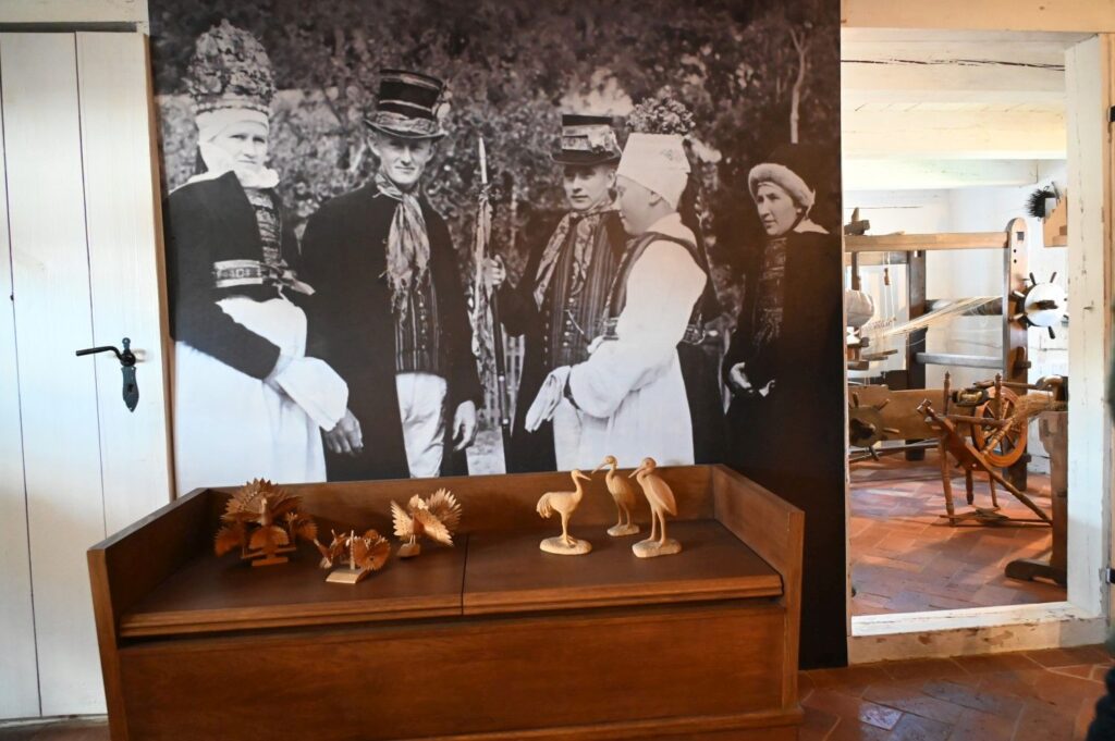 Wnętrze ekspozycji w chacie, w tle archiwalne zdjęcie mieszkańców Jamna w strojach ludowych, na pierwszym planie drewniane rzeźby ptaków (kliknięcie powiększy zdjęcie).