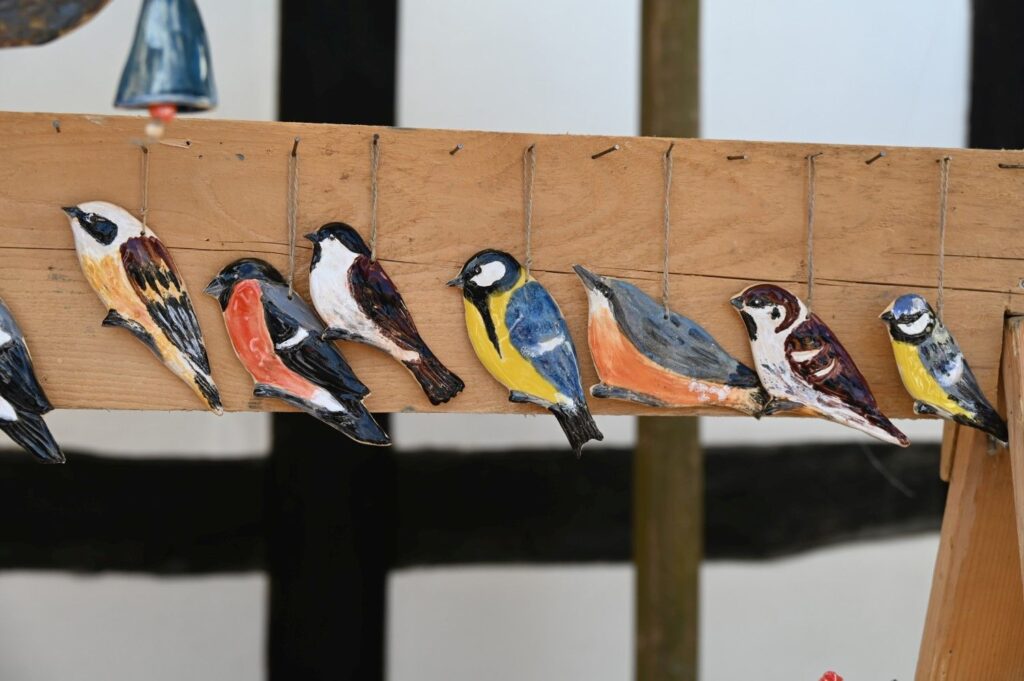 Drewniane, ręcznie malowane figurki ptaków zawieszone w rzędzie na drewnianej desce (kliknięcie powiększy zdjęcie).
