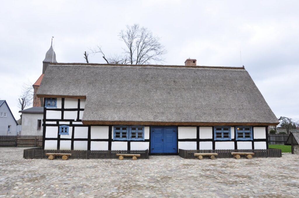 Widok zewnętrzny zabytkowej chaty o konstrukcji szachulcowej z bielonymi ścianami i dachem krytym strzechą (kliknięcie powiększy zdjęcie).