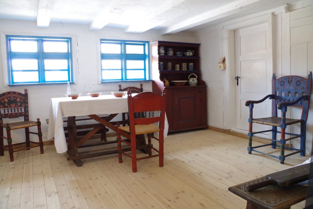 Rekonstrukcja jadalni w wiejskim domu z drewnianym stołem, krzesłami i kredensem przy ścianie (kliknięcie powiększy zdjęcie).