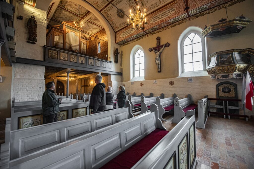 Zwiedzający we wnętrzu zabytkowego kościoła; widoczne drewniane ławy, empora i ołtarz (kliknięcie powiększy zdjęcie).