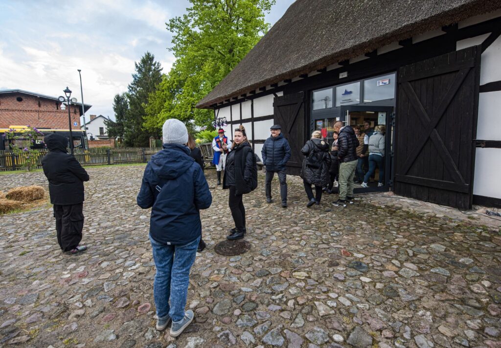 Uczestnicy Nocy Muzeów w Zagrodzie Jamneńskiej zgromadzeni przed zabytkową, szachulcową stodołą na terenie skansenu; na pierwszym planie brukowany dziedziniec (kliknięcie powiększy zdjęcie).