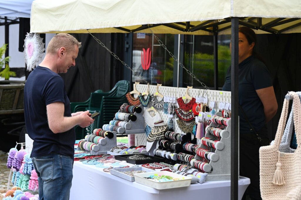 Stoisko z ręcznie robioną biżuterią i dodatkami, przy którym klient ogląda prezentowane wyroby (kliknięcie powiększy zdjęcie).