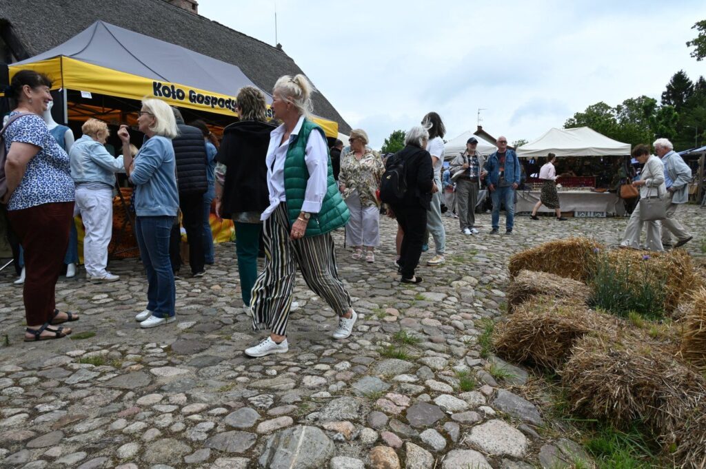 Uczestnicy jarmarku spacerujący po brukowanym terenie skansenu pomiędzy stoiskami (kliknięcie powiększy zdjęcie).