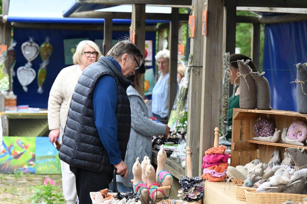 Odwiedzający oglądający rękodzieło i zabawki na stoisku jarmarkowym ustawionym w drewnianej zabudowie (kliknięcie powiększy zdjęcie).