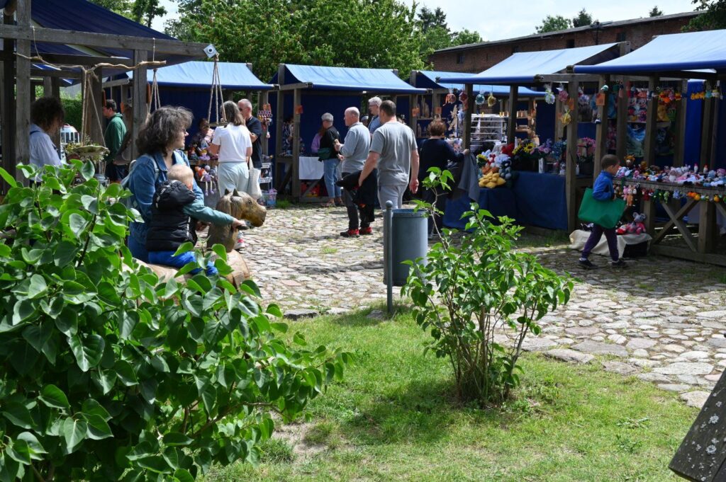 Widok alei jarmarcznej z ustawionymi stoiskami i spacerującymi uczestnikami wydarzenia (kliknięcie powiększy zdjęcie).