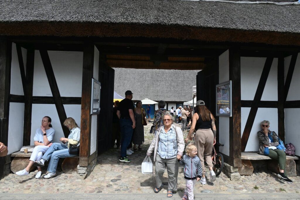 Zwiedzający wchodzący i odpoczywający w podcieniach tradycyjnej chałupy na terenie skansenu (kliknięcie powiększy zdjęcie).