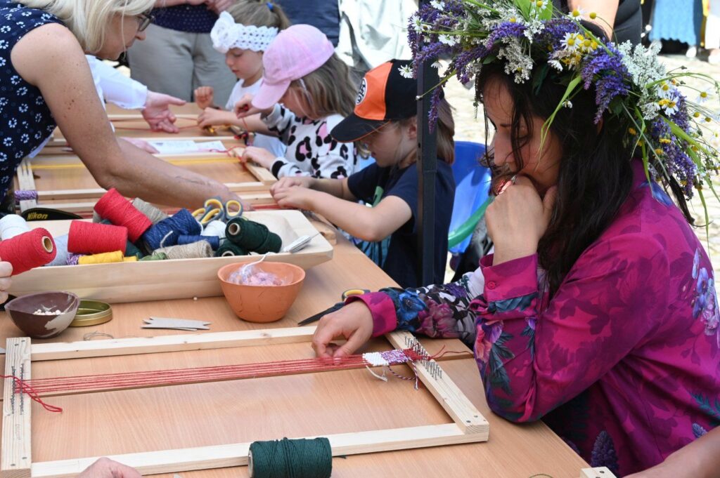 Warsztaty rękodzielnicze dla dzieci i dorosłych przy długim stole z materiałami plastycznymi (kliknięcie powiększy zdjęcie).