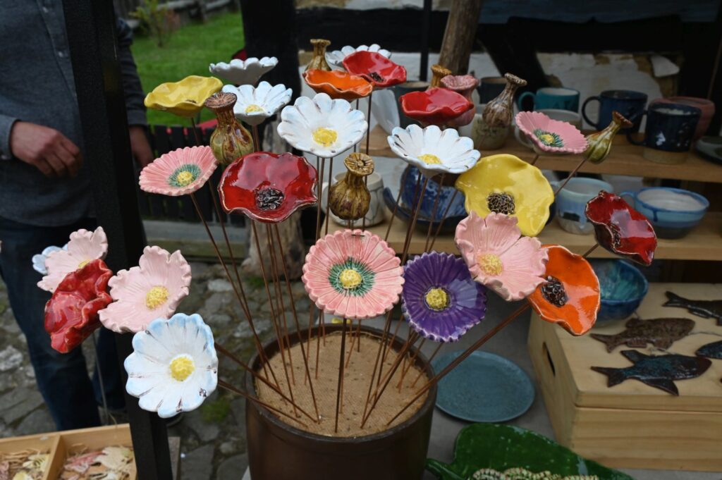 Kolorowe ceramiczne kwiaty na metalowych prętach prezentowane na stoisku rękodzielniczym podczas jarmarku (kliknięcie powiększy zdjęcie).