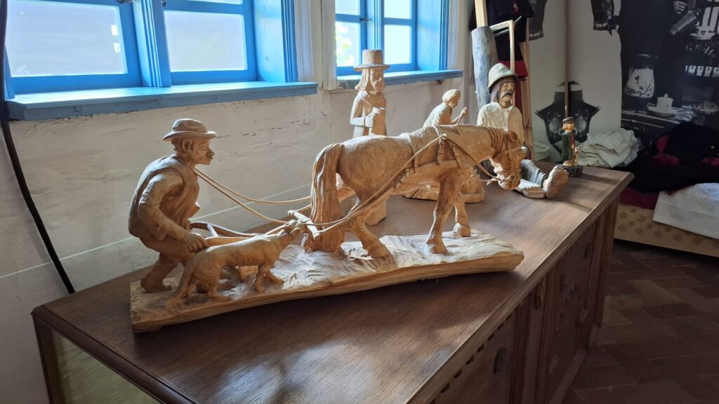 Drewniana rzeźba ukazująca pracę rolnika z koniem i narzędziami, prezentowana jako element wystawy stałej w chałupie (kliknięcie powiększy zdjęcie).