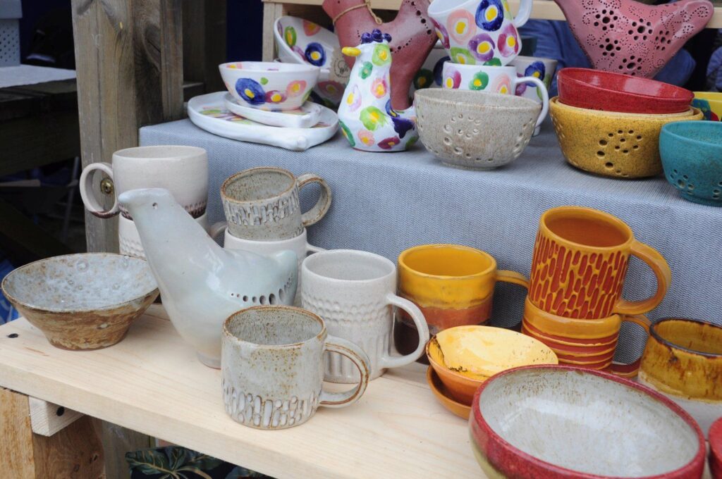 Stoisko z ręcznie wykonaną ceramiką – kubkami, misami i dzbankami ustawionymi na drewnianej półce (kliknięcie powiększy zdjęcie).