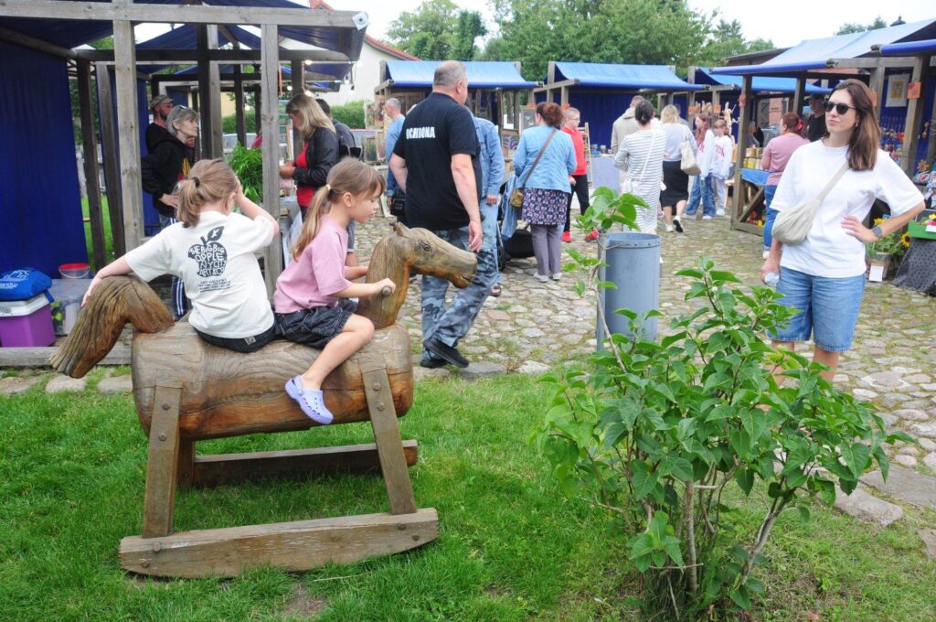 Dzieci bawią się na drewnianym koniku na placu podczas Jarmarku Jamneńskiego (kliknięcie powiększy zdjęcie).