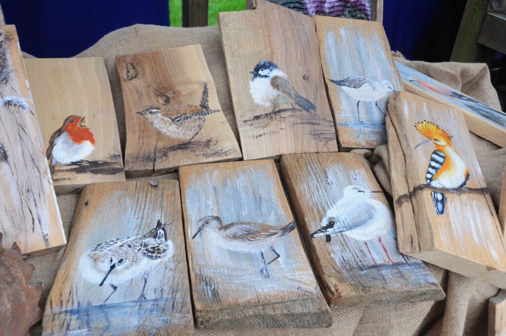 Drewniane deski ozdobione malowanymi wizerunkami ptaków prezentowane na stoisku z rękodziełem (kliknięcie powiększy zdjęcie).
