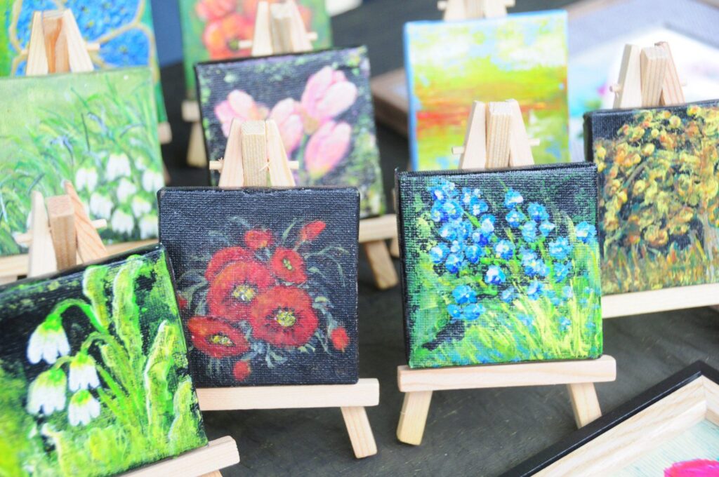 Małe obrazy z motywami kwiatów ustawione na sztalugach na stoisku z rękodziełem artystycznym (kliknięcie powiększy zdjęcie).