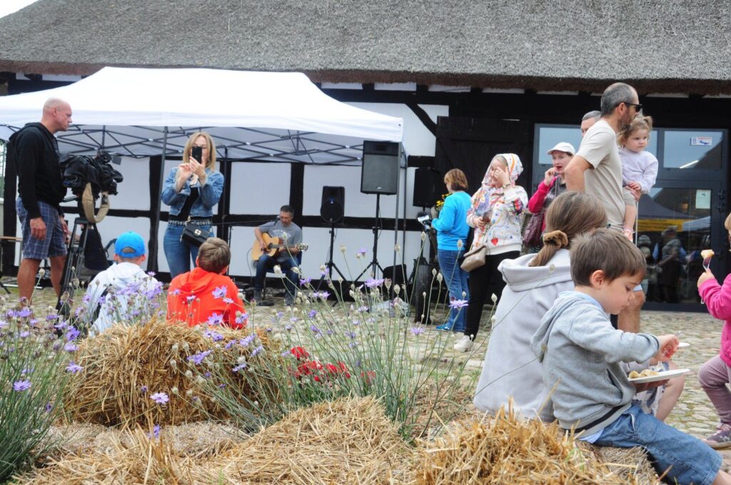 Scena jarmarku z muzyką na żywo, gdzie odwiedzający stoją i słuchają występu artysty grającego na gitarze (kliknięcie powiększy zdjęcie).