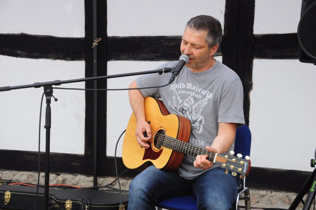 Muzyk siedzący przy mikrofonie gra na gitarze podczas koncertu na Jarmarku Jamneńskim (kliknięcie powiększy zdjęcie).