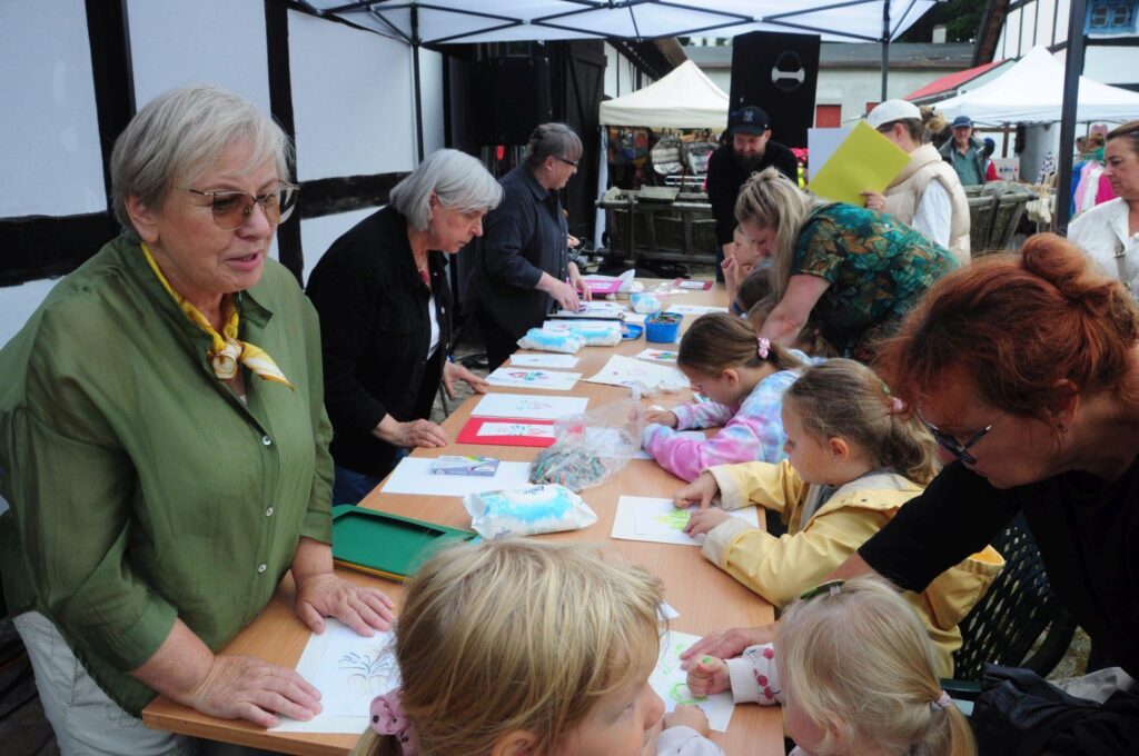 Stoisko warsztatowe dla dzieci, przy którym prowadzące pomagają najmłodszym w pracach plastycznych (kliknięcie powiększy zdjęcie).