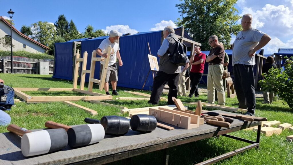 Uczestnicy wydarzenia zgromadzeni wokół stołu z narzędziami i drewnianymi elementami konstrukcji (kliknięcie powiększy zdjęcie)