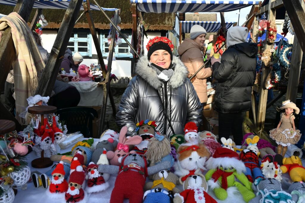 Stoisko z ręcznie wykonanymi lalkami i maskotkami, za którym stoi uśmiechnięta wystawczyni podczas Jarmarku Jamneńskiego (kliknięcie powiększy zdjęcie).