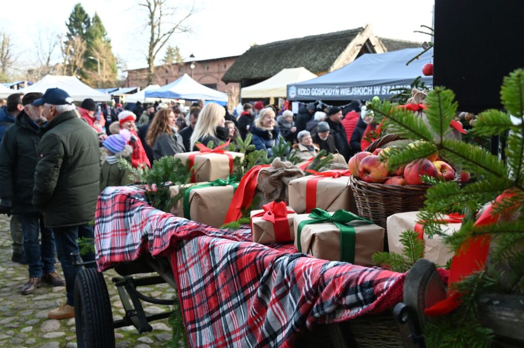 Stoiska jarmarczne z ozdobami i paczkami prezentowymi na tle licznie zgromadzonych odwiedzających (kliknięcie powiększy zdjęcie).