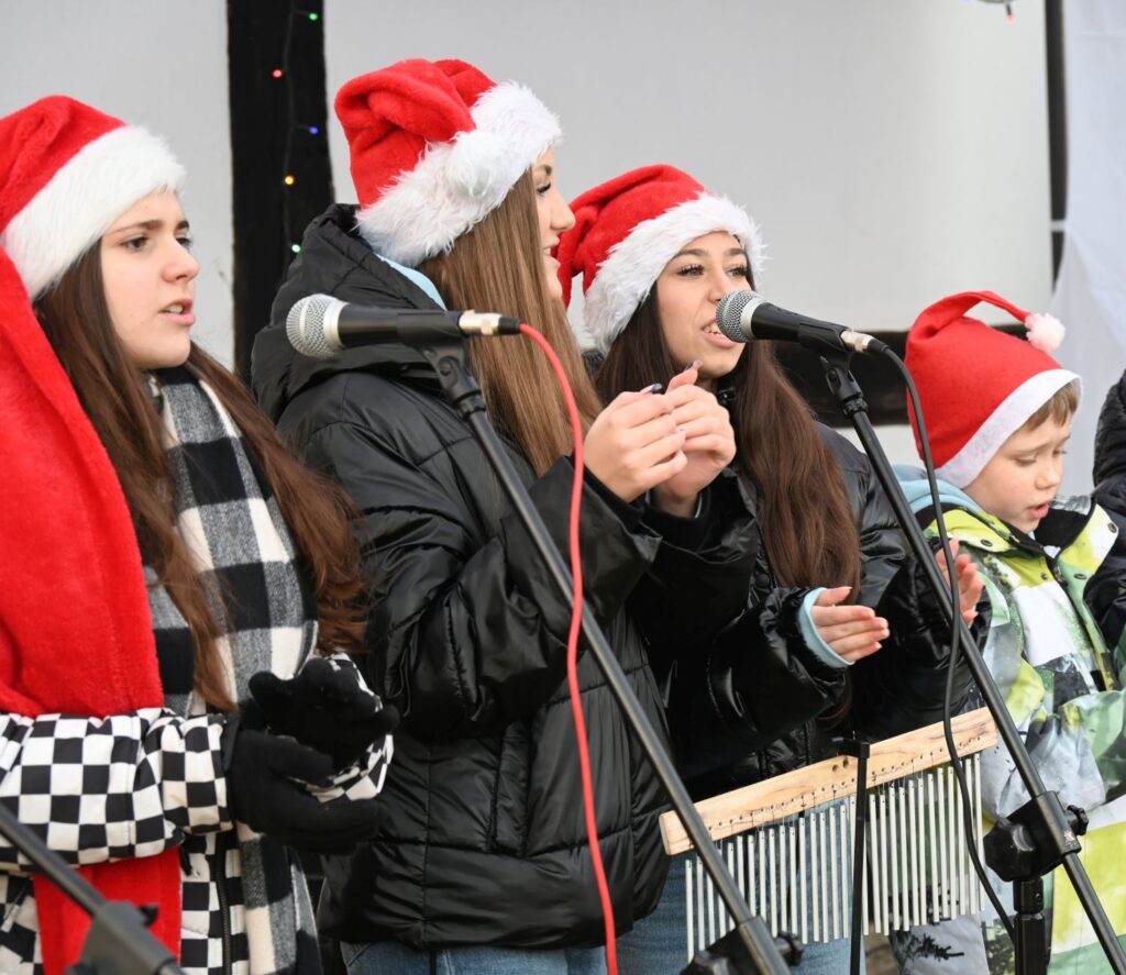 Występ młodzieżowej grupy wokalnej w czapkach mikołajowych na scenie podczas jarmarku jamneńskiego (kliknięcie powiększy zdjęcie).