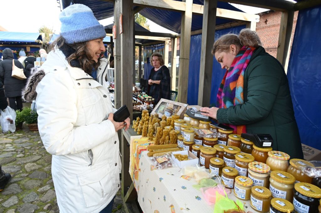 Kobieta oglądająca stoisko z miodami i świecami z wosku pszczelego na jarmarku jamneńskim (kliknięcie powiększy zdjęcie).