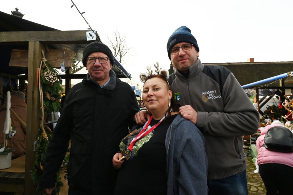Trzy osoby pozujące do zdjęcia na tle stoiska jarmarkowego podczas jarmarku jamneńskiego (kliknięcie powiększy zdjęcie).