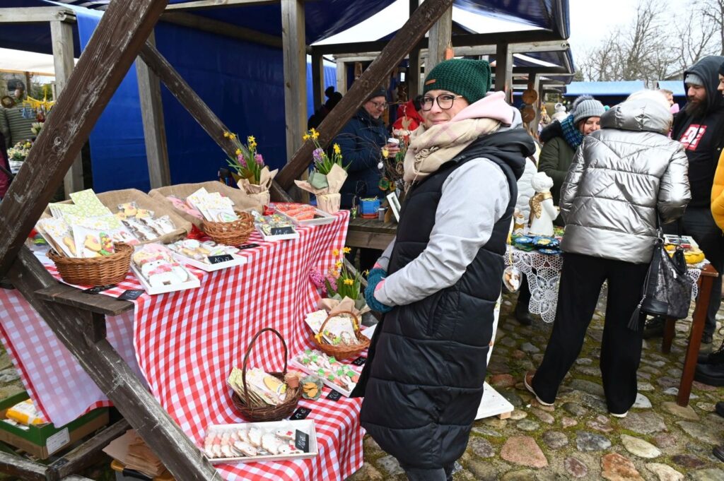 Kobieta ogląda wyroby i ozdoby świąteczne wyłożone na stole przykrytym czerwono-białym obrusem (kliknięcie powiększy zdjęcie).