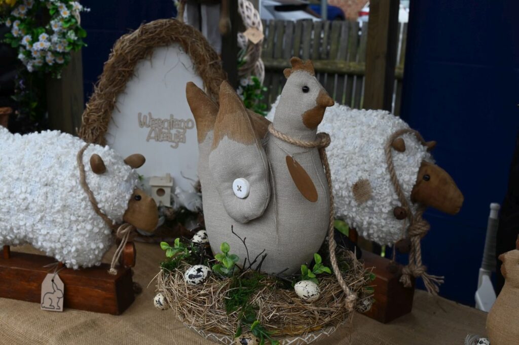 Wielkanocne dekoracje z tkaniny przedstawiające owce i kurę ustawione na stole wśród gniazd i ozdobnych jajek (kliknięcie powiększy zdjęcie).