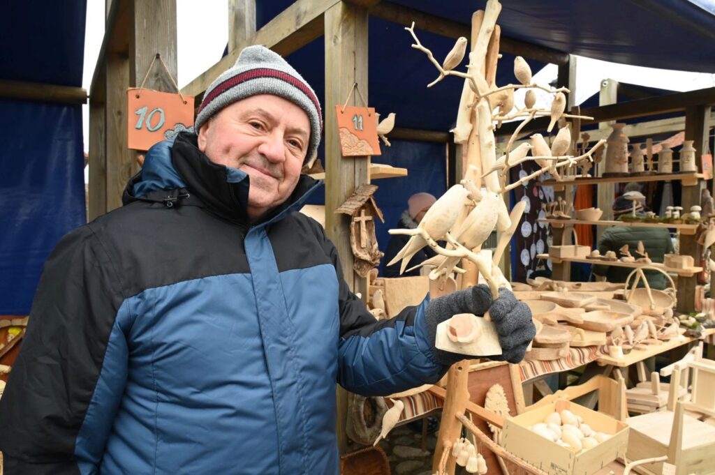 Rzemieślnik prezentuje drewniane zabawki i rzeźby wystawione na stoisku (kliknięcie powiększy zdjęcie).