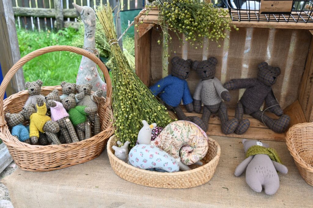 Ręcznie szyte maskotki i pluszowe zabawki ułożone w koszach i drewnianej skrzyni na stoisku z rękodziełem (kliknięcie powiększy zdjęcie).