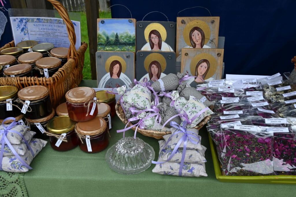 Stoisko z domowymi przetworami, suszonymi ziołami, pachnącymi woreczkami oraz ikonami ustawionymi na tle niebieskiej tkaniny (kliknięcie powiększy zdjęcie).