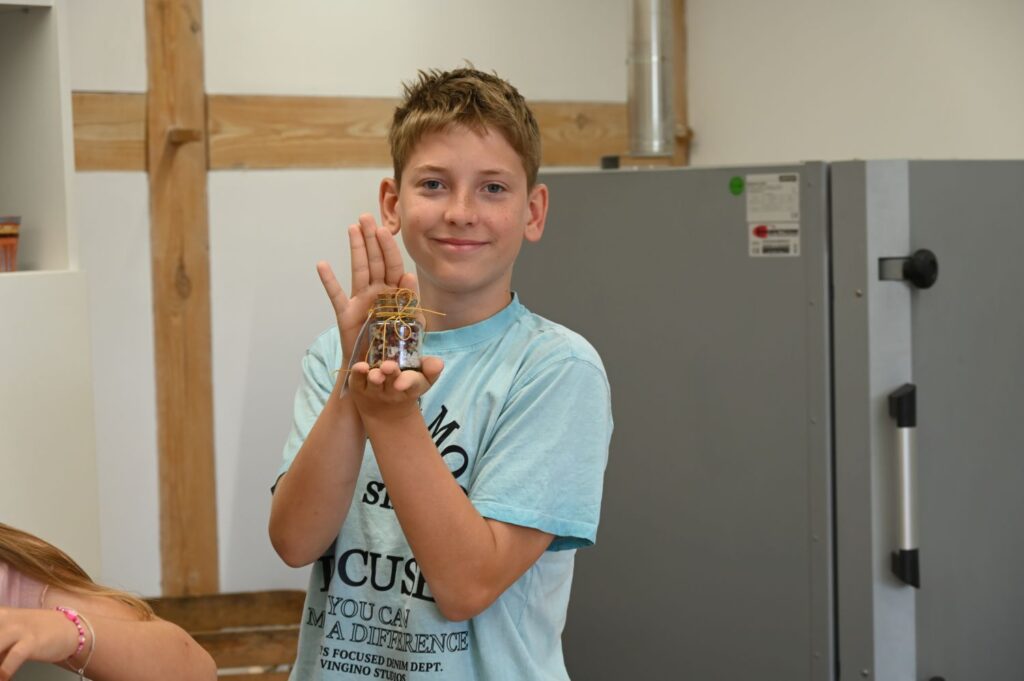 Chłopiec pokazuje słoiczek z przygotowaną mieszanką ziół podczas warsztatów odbywających się w pracowni (kliknięcie powiększy zdjęcie).