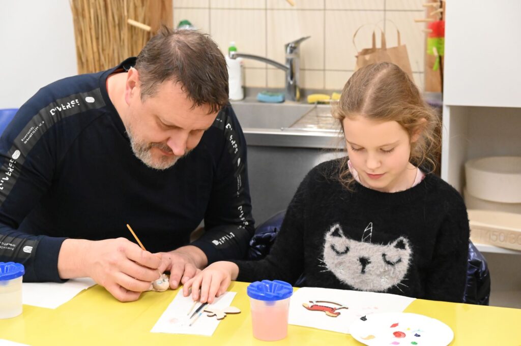 Mężczyzna i dziewczynka siedzą przy stole i wspólnie malują świąteczne wzory na papierze (kliknięcie powiększy zdjęcie).