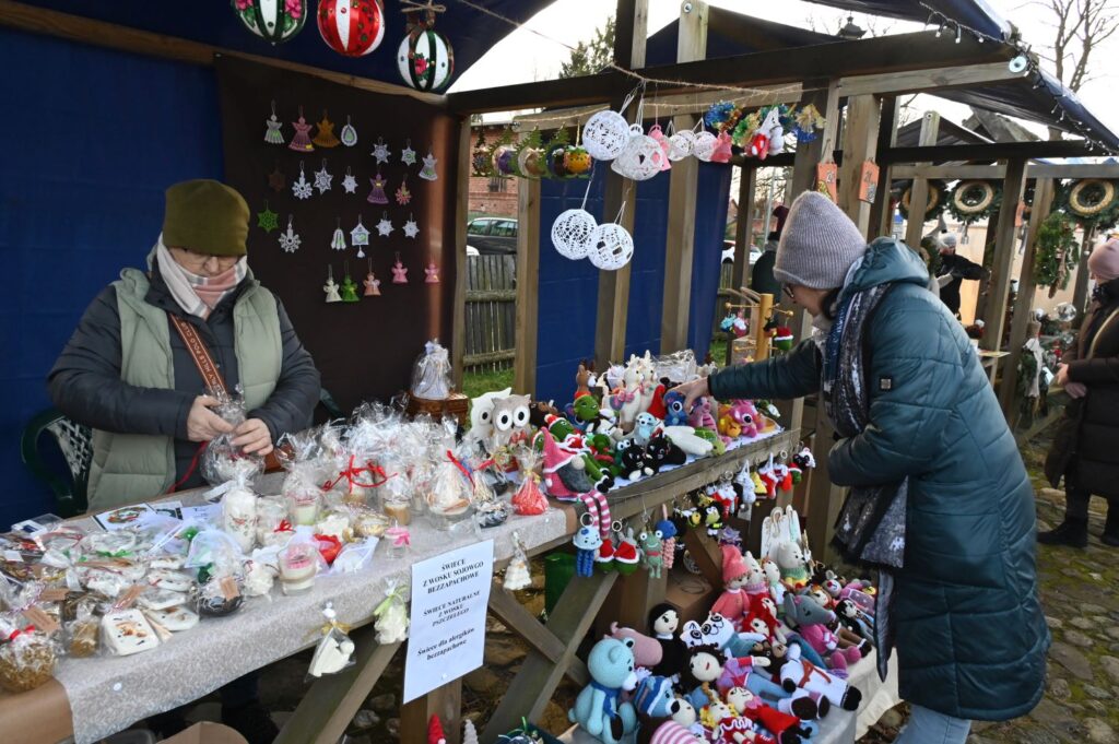 Stoisko z ozdobami świątecznymi i rękodziełem, przy którym kobieta wybiera dekoracje (kliknięcie powiększy zdjęcie).