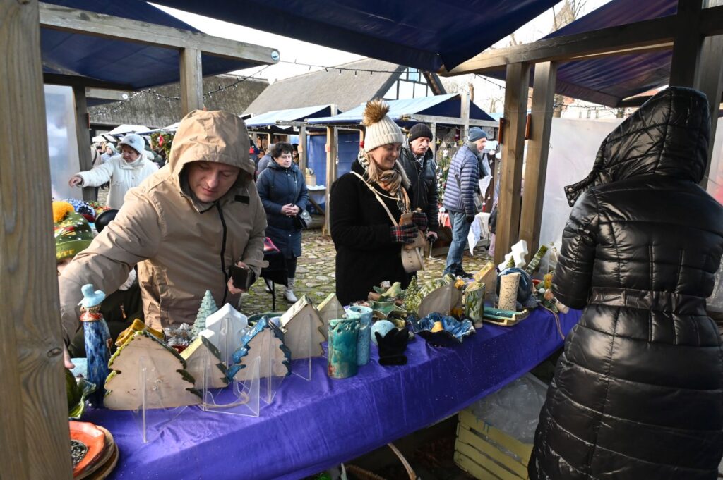 Stoisko z rękodziełem, przy którym sprzedawczyni układa ozdoby, a klienci oglądają produkty (kliknięcie powiększy zdjęcie).