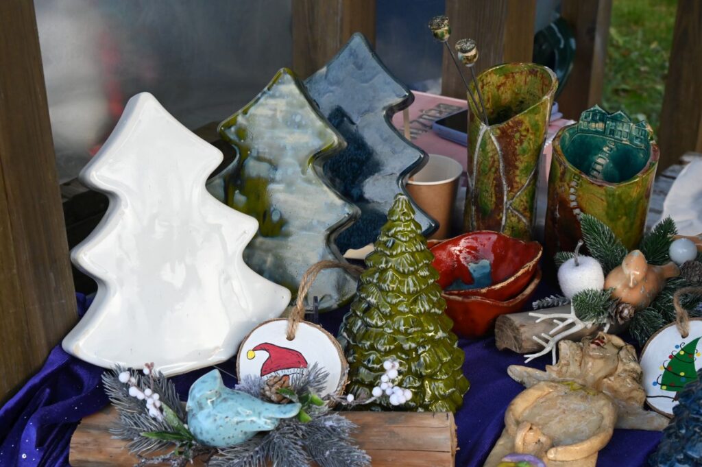 Zbliżenie na ceramiczne i szklane ozdoby świąteczne w kształcie choinek ustawione na stole (kliknięcie powiększy zdjęcie).
