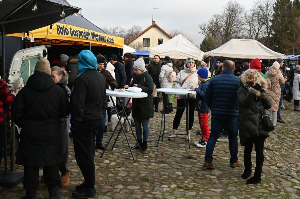 Tłum odwiedzających przy stoisku gastronomicznym na brukowanym placu podczas jarmarku bożonarodzeniowego (kliknięcie powiększy zdjęcie)