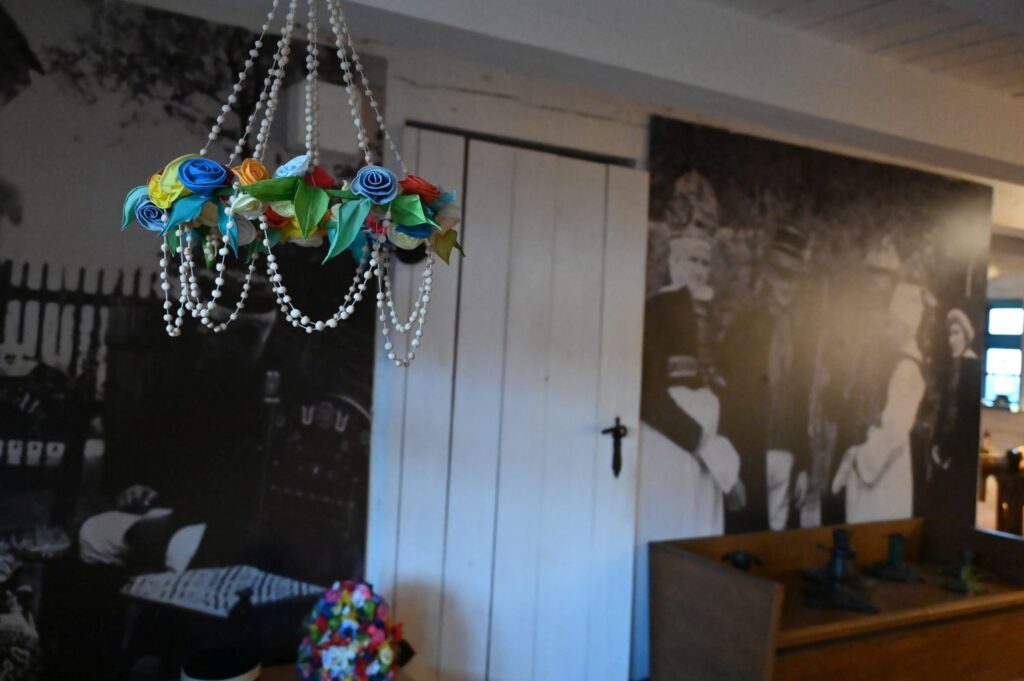 Wnętrze izby muzealnej z wiszącą ozdobą i archiwalnym zdjęciem Jamneńczyków na ścianie (kliknięcie powiększy zdjęcie).